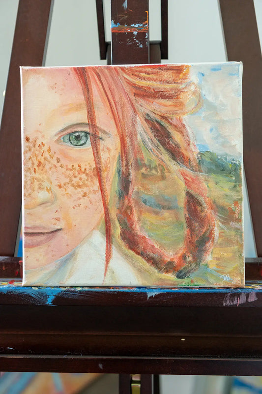 “Freckles” original acrylic painting by Danita Brooks, featuring a close-up portrait of a freckled girl with red hair, shown on an easel