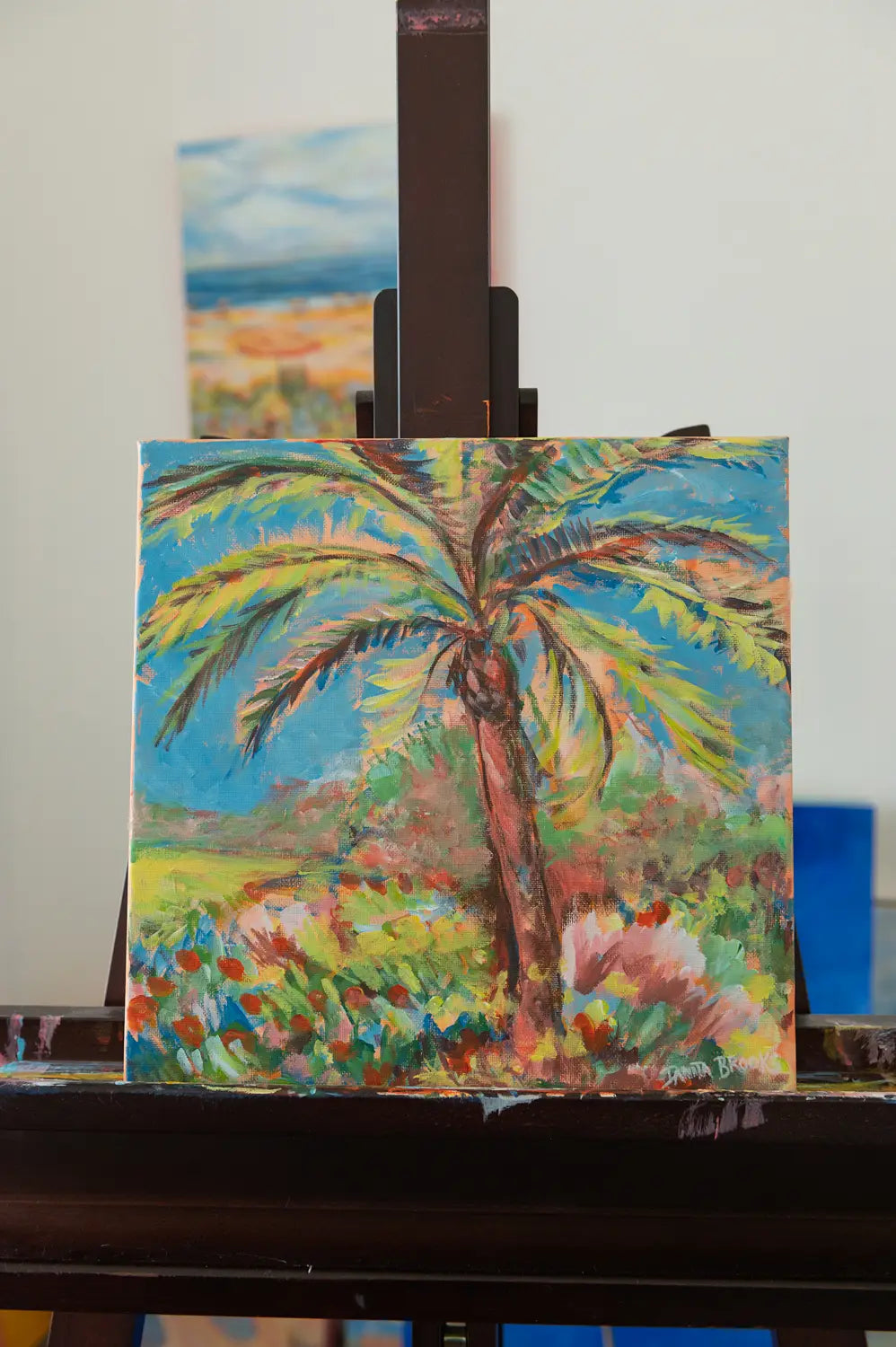 Original palm tree painting titled "Midday Blues" by Danita Brooks, shown here sitting on the easel and displayed in natural light