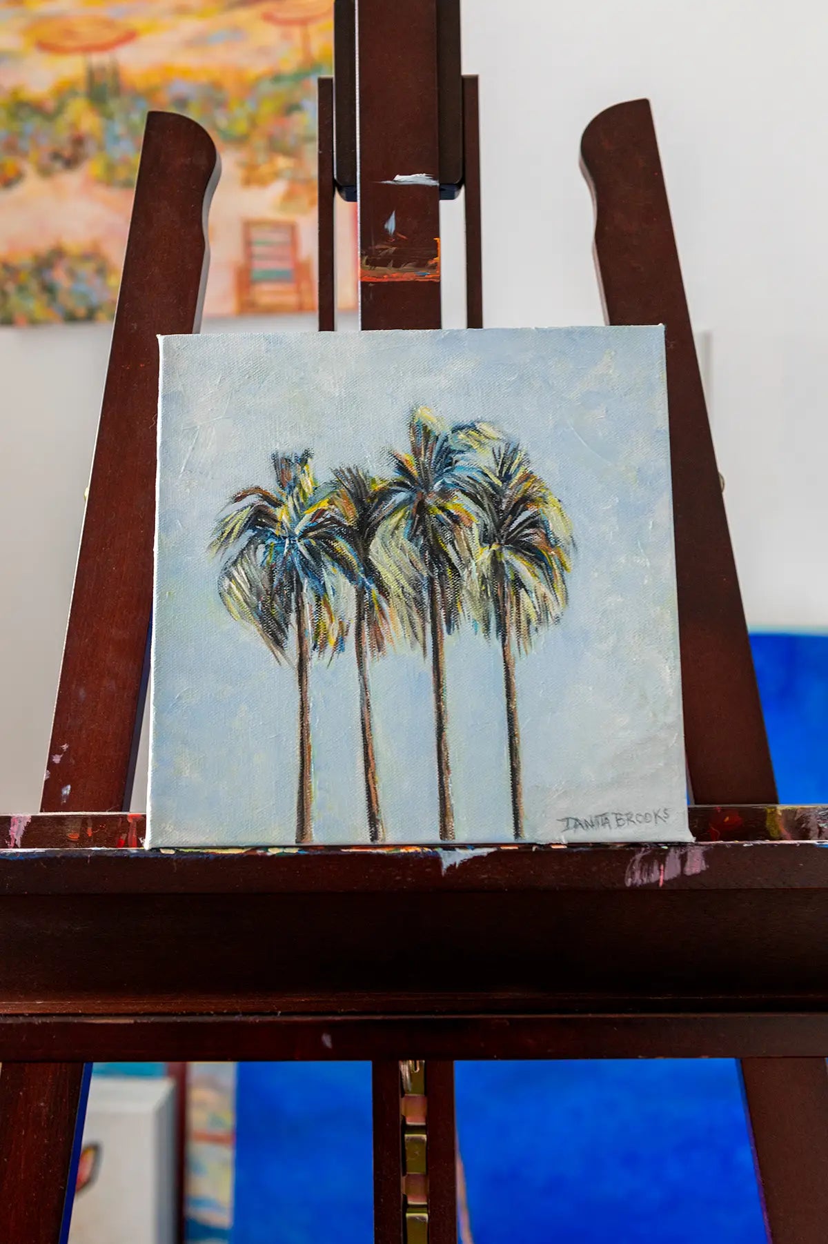 Original palm tree oil painting titled "Four Palms" by Danita Brooks, displayed on an easel with natural coastal light