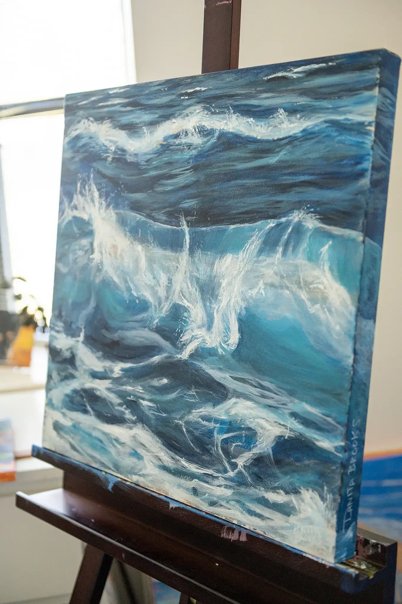 Side view of acrylic wave painting showing signature on the bottom corner and side of "Nanosecond" original acrylic painting on 1.5-inch gallery wrapped canvas - shown on Danita's easel in her studio