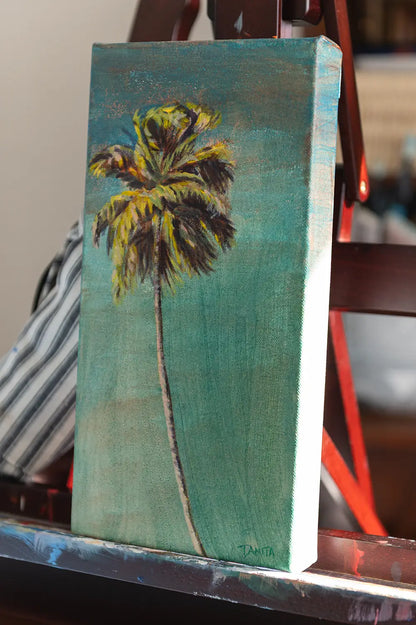 Angled view of "The Long Way Home" on an easel, showing the palm tree painting and the right edge of the stretched canvas.