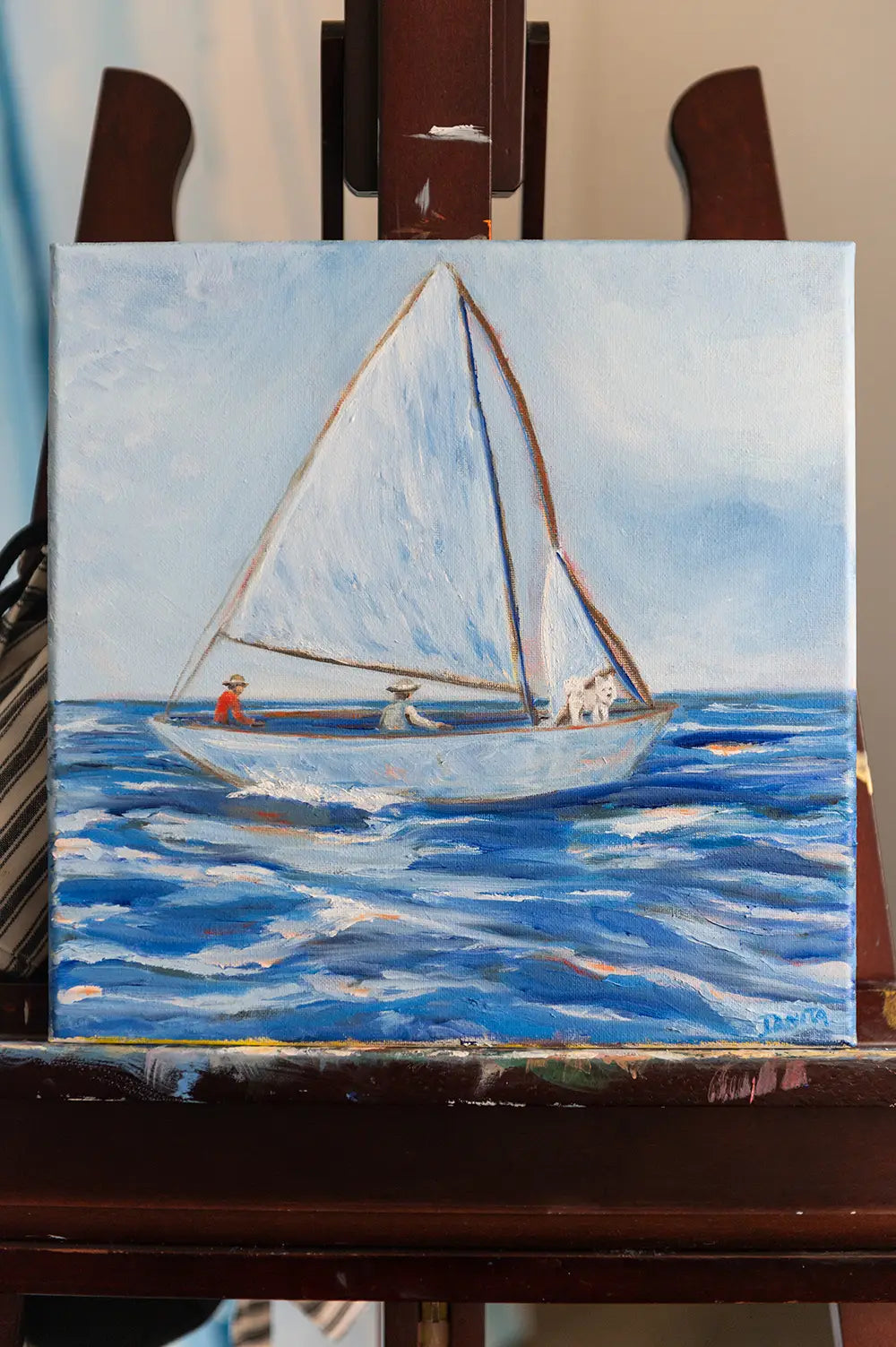 "First Mate" small oil painting by Danita Brooks on a wooden easel, depicting two people and a white dog in a sailboat on blue ocean waves.