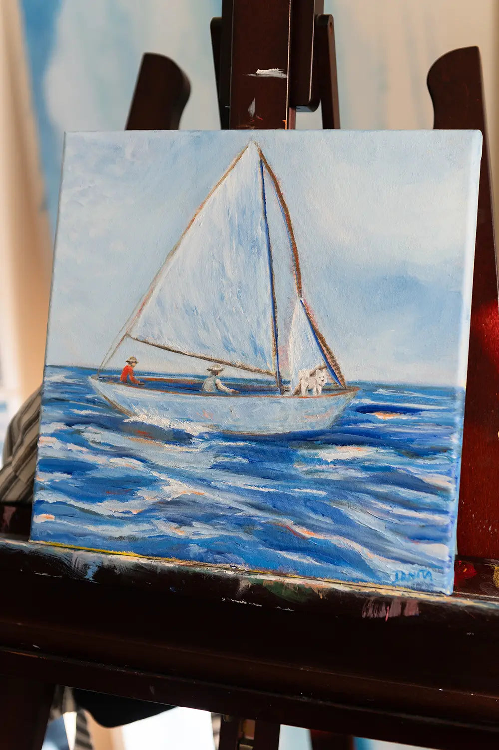 Angled view of "First Mate" oil painting on a studio easel, showing the full sailboat painting and the canvas edge.