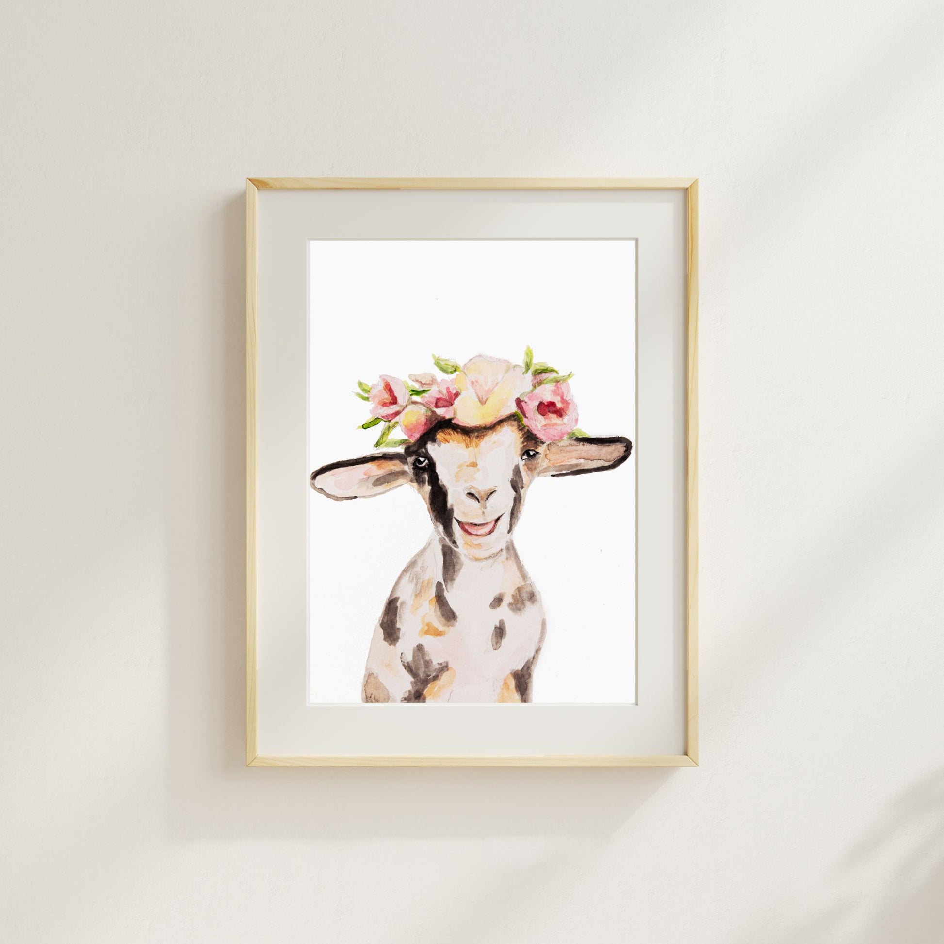Framed artwork from Danita Brooks Studio of a watercolor goat with a floral crown art print on a white wall