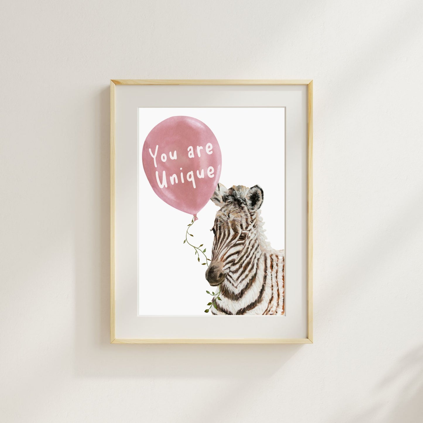 Framed artwork with a zebra holding a pink balloon that says 'You are Unique' on a white wall.