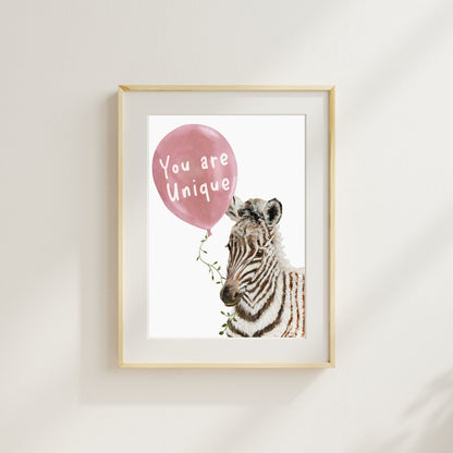 Framed artwork with a zebra holding a pink balloon that says 'You are Unique' on a white wall.