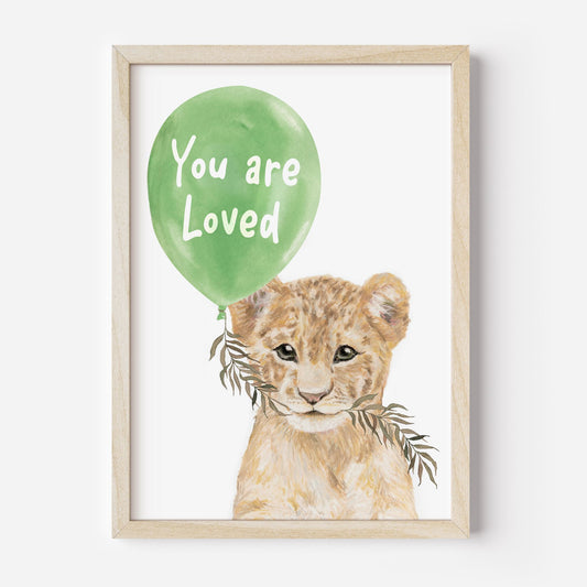 Framed artwork of a lion cub holding a green balloon with 'You are Loved' text on a white background.